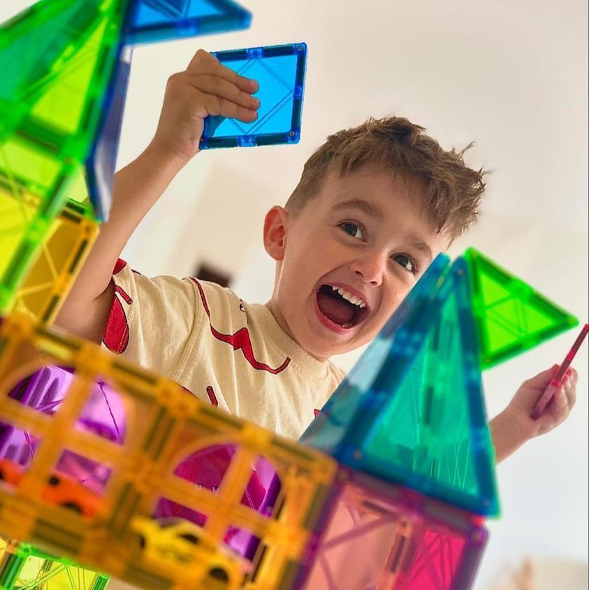 Jongen lacht achter zijn bouwwerk van magnetische tegels